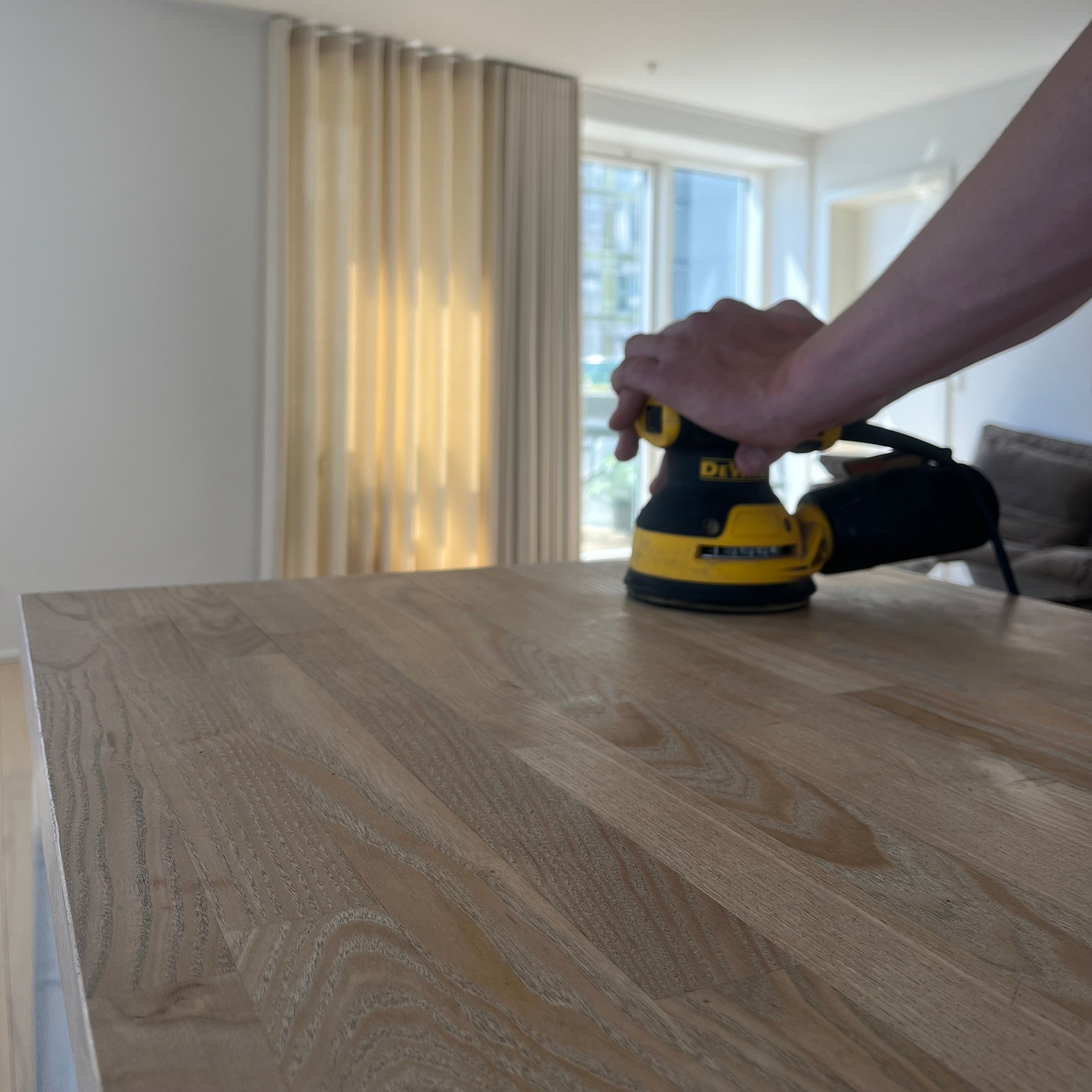 Dewalt excentersliber i gang med at slibe køkkenø i Isbjerget på Aarhus Ø – præcis og nænsom slibning af træoverflade som forberedelse til oliebehandling og finish.